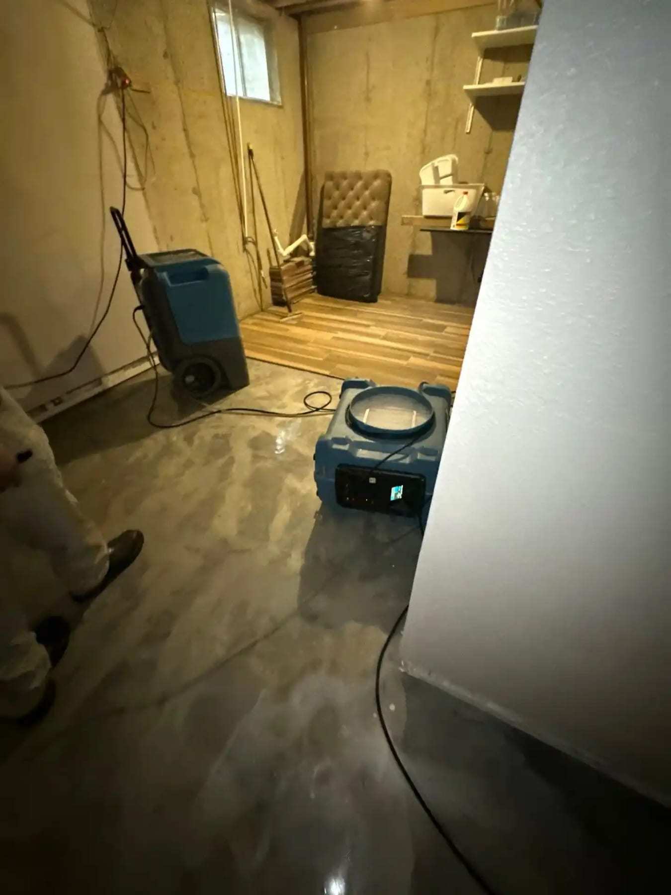 Basement with a dehumidifier and air mover on a wet concrete floor